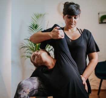 Masajista asistiendo a su clienta a estirar su torso, brazo y cuello para eliminar tensiones musculares durante masajes descontracturantes.