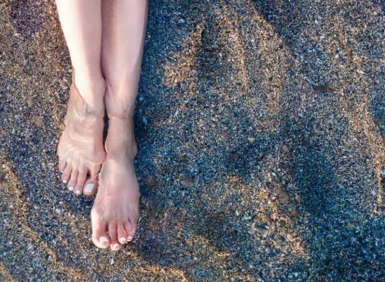 Mujer limpiando la piel de sus pies, sumergiéndolos en un río y masajeando sus plantas con piedras y la arena.