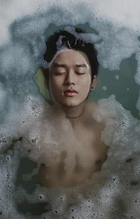 Hombre joven sumergido en una bañera especial con productos nutritivos de terapia mientras recibe Watsu y masaje de burbujas.